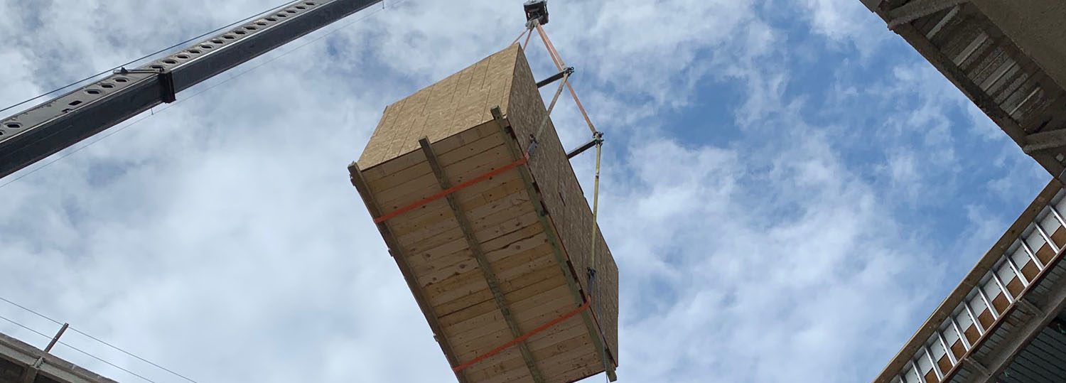 A wooden crate being hoisted by a crane into a building with a blue sky.
